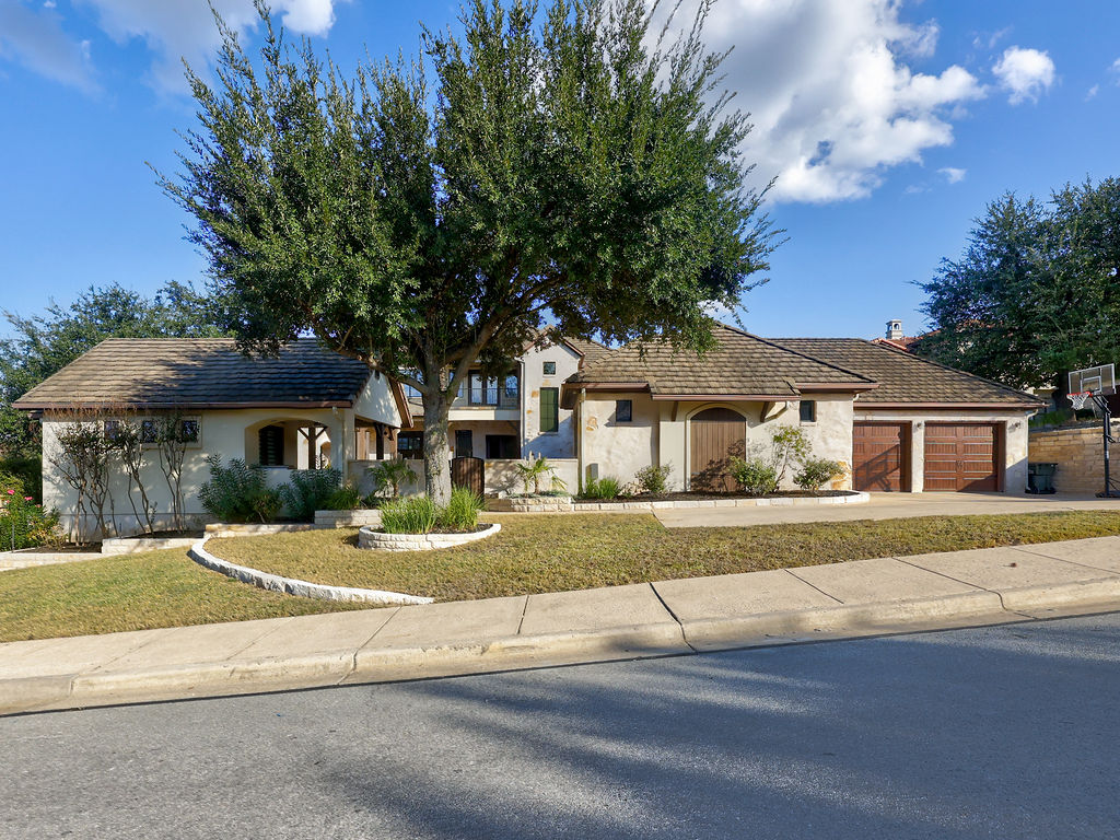11805 Pleasant Panorama View Austin, TX 78738 - Photo 5 of 40 Nestled behind the graceful canopy of a mature oak tree, this estate offers a commanding street presence that seamlessly blends natural beauty with architectural grandeur.