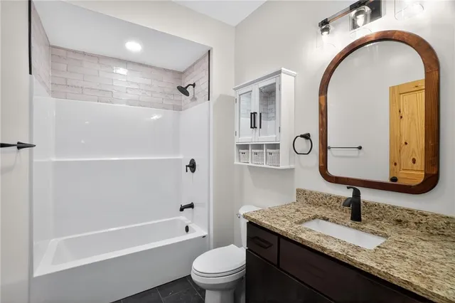 a bathroom with a granite countertop toilet a sink a mirror and bathtub