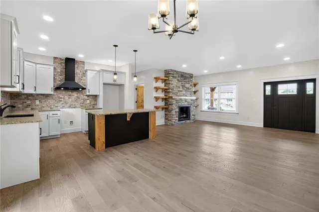 a large kitchen with stainless steel appliances kitchen island granite countertop a stove a refrigerator a sink dishwasher and a fireplace with wooden floor