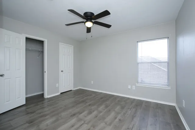 an empty room with wooden floor ceiling fan and window