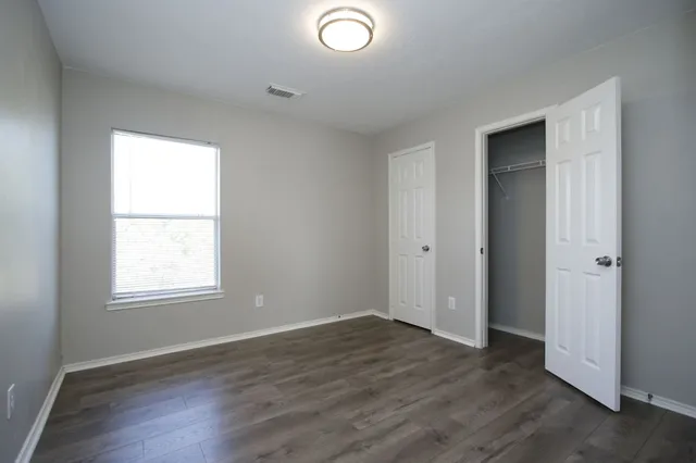 a view of an empty room with wooden floor and window