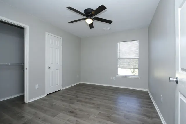 an empty room with wooden floor ceiling fan and window