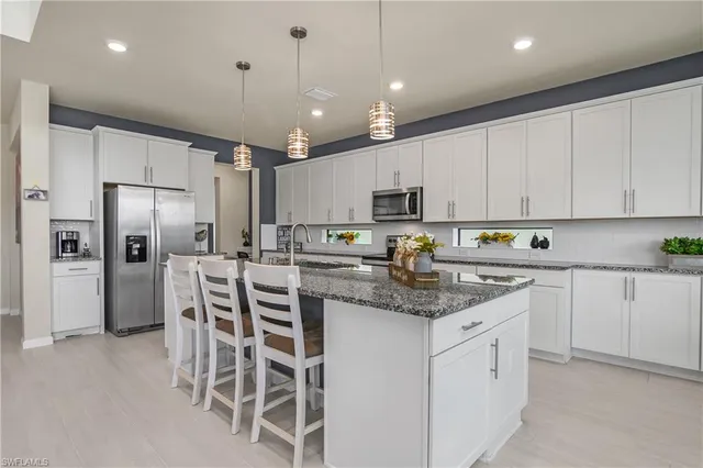 a kitchen with stainless steel appliances granite countertop a refrigerator a sink dishwasher a stove and white cabinets with wooden floor