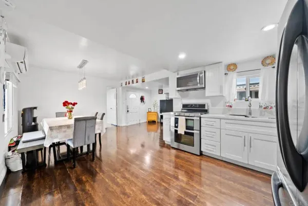 a kitchen with stainless steel appliances granite countertop a stove top oven a refrigerator a dining table and chairs with wooden floor