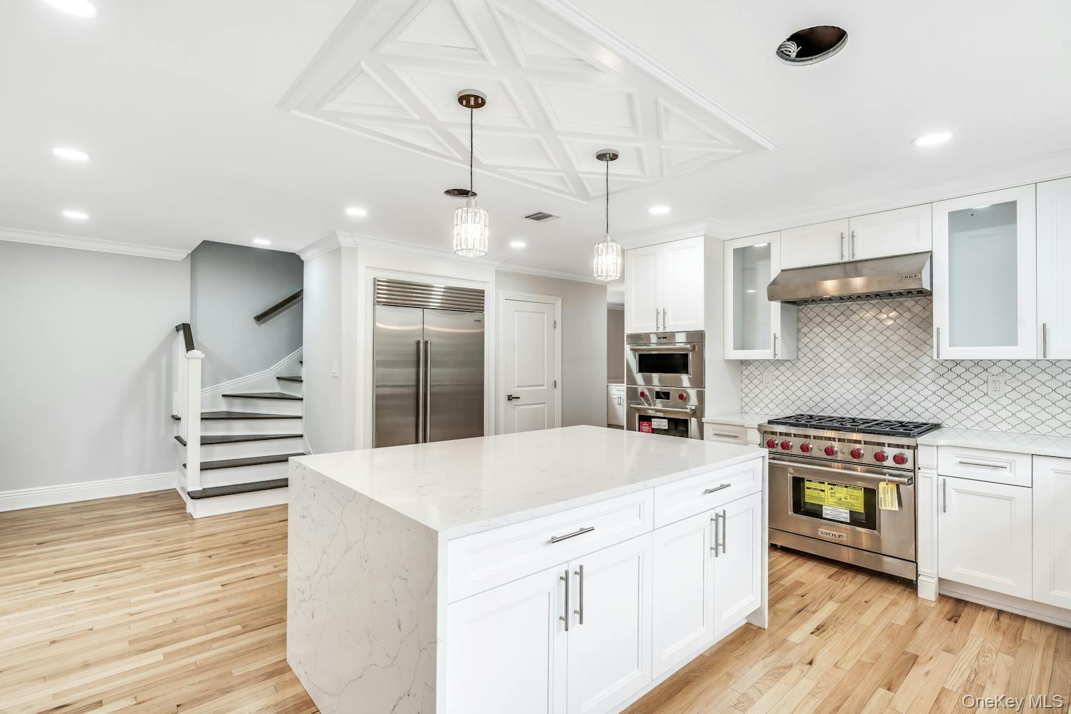 539 Split Rock Road Syosset, NY 11791 - Photo 15 of 40 Kitchen featuring decorative backsplash, high end appliances, light wood-type flooring, under cabinet range hood, and white cabinets