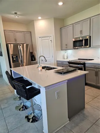 a kitchen with stainless steel appliances a sink a stove a refrigerator cabinets and chairs