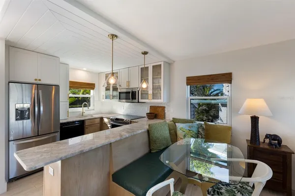 a kitchen with stainless steel appliances granite countertop a sink a stove a refrigerator white cabinets a dining table and chairs