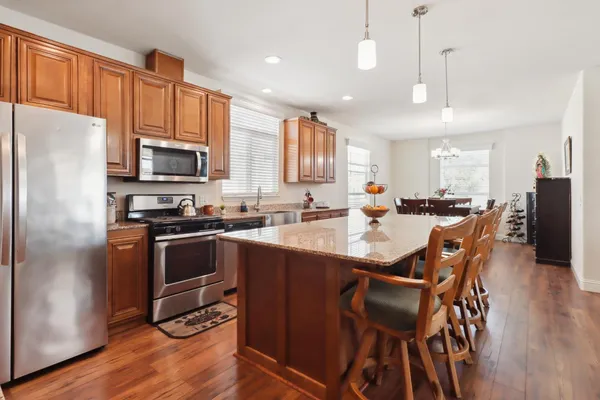 a kitchen with stainless steel appliances kitchen island granite countertop a refrigerator a stove a sink a dining table and chairs with wooden floor