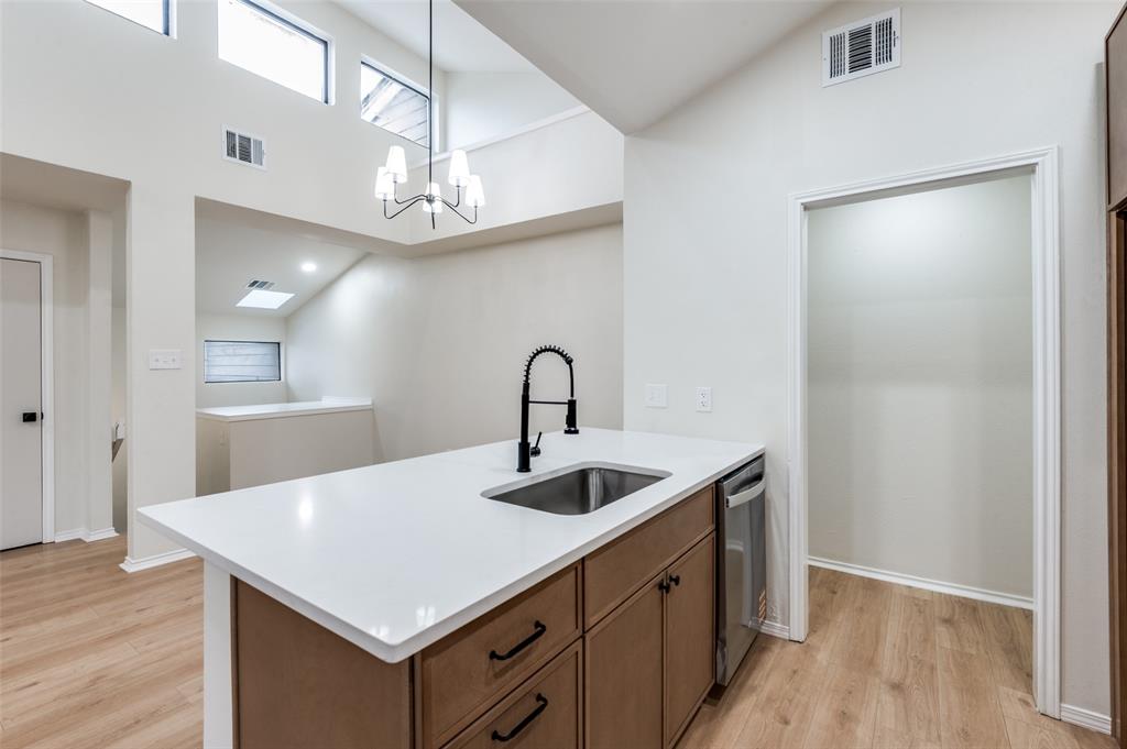 17490 Meandering Way, Unit 2202 Dallas, TX 75252 - Photo 17 of 24 Kitchen island featuring a white countertop, undermount sink with a matte black faucet, and wood-finish cabinetry with black hardware