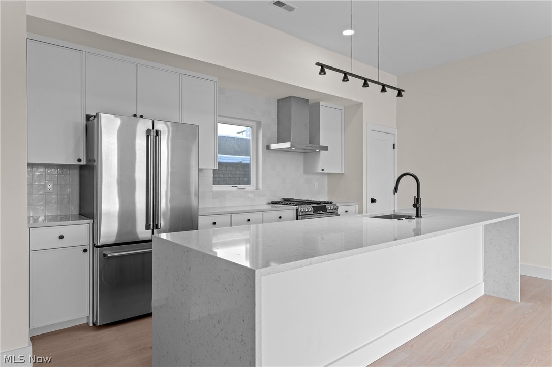 Kitchen featuring stainless steel appliances, light wood finished floors, white cabinets, decorative backsplash, and track lighting
