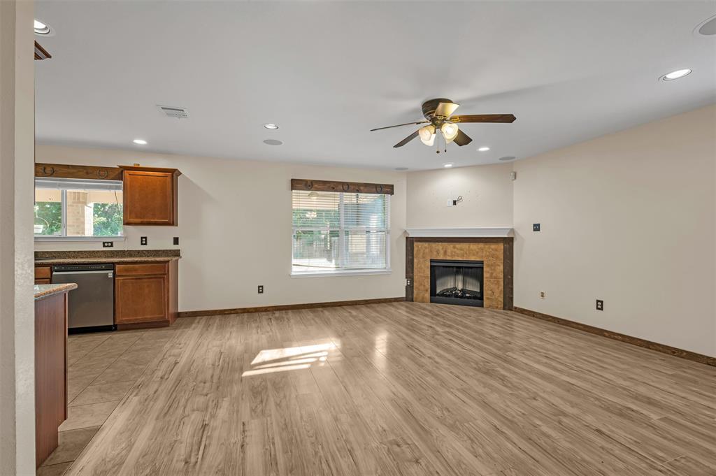 9017 Graywolf Ridge Trail Fort Worth, TX 76244 - Photo 7 of 27 Unfurnished living room with ceiling fan, a tiled fireplace, and light hardwood / wood-style floors