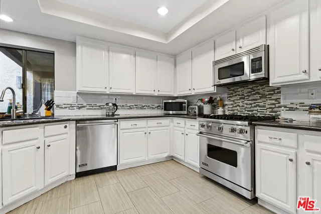 a kitchen with stainless steel appliances granite countertop a stove a sink and white cabinets