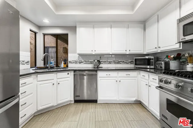 a kitchen with granite countertop white cabinets stainless steel appliances a sink and a window
