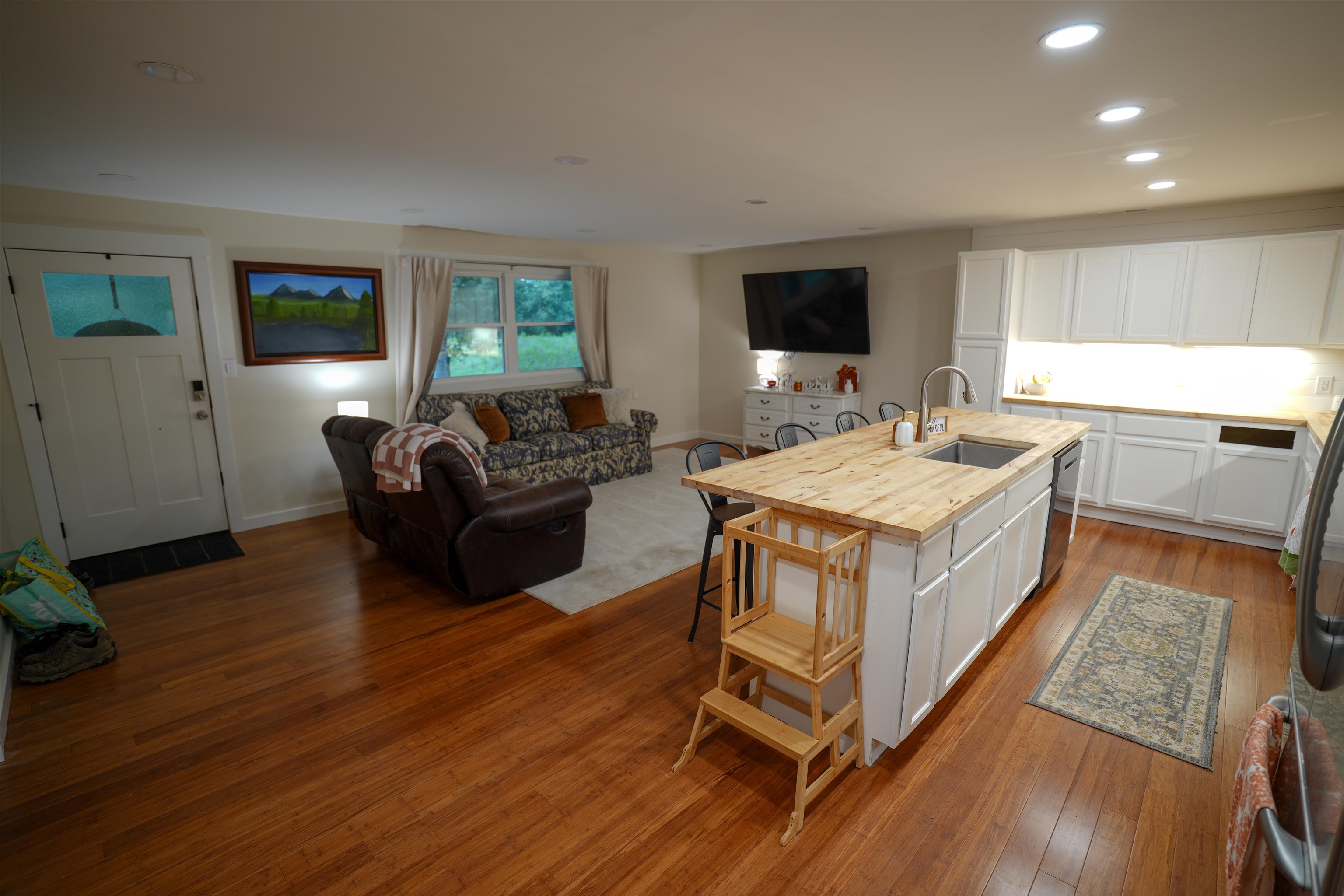 Hardwood flooring throughout, recessed lighting, white kitchen cabinetry, wood-finish countertops, and a kitchen island with an undermount sink