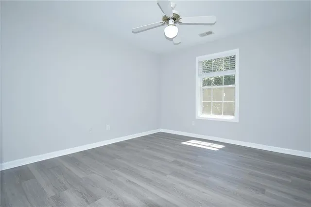 an empty room with wooden floor fan and windows