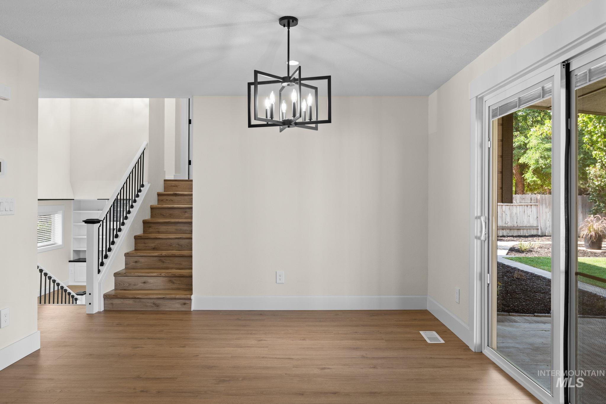 1675 Country Terrace Way Meridian, ID 83642 - Photo 8 of 50 Wood-finish flooring throughout, modern black chandelier, white walls, and a sliding glass door providing exterior access