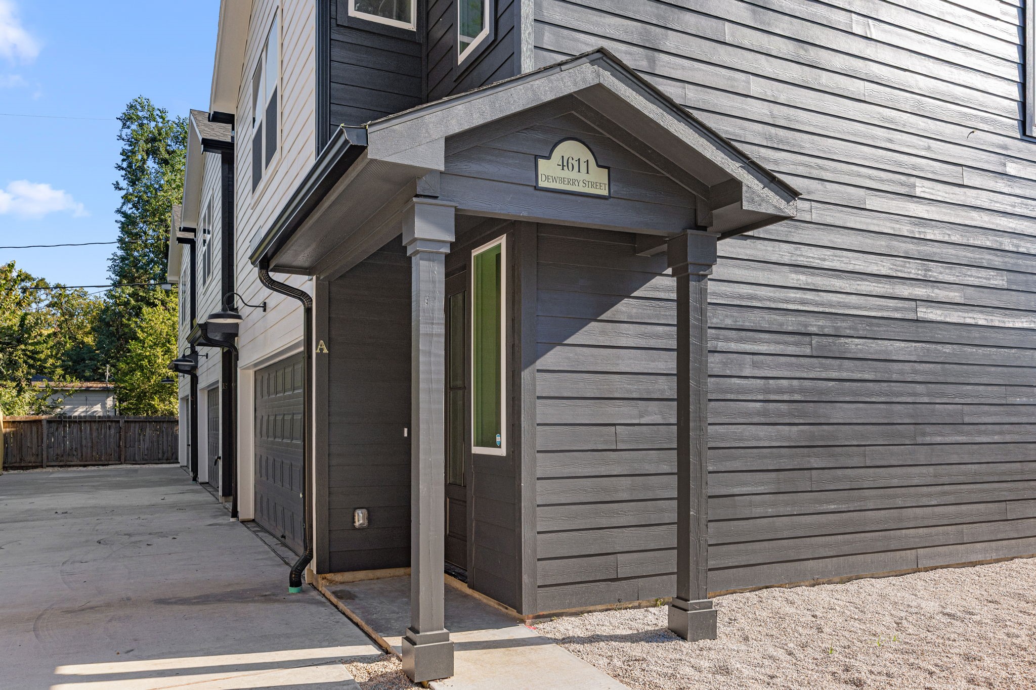 4611 Dewberry Street, Unit C Houston, TX 77021 - Photo 30 of 34 This photo showcases a modern townhouse with a sleek dark exterior, featuring a covered entrance and attached garage. The driveway is spacious, and there's a wooden fence providing privacy.