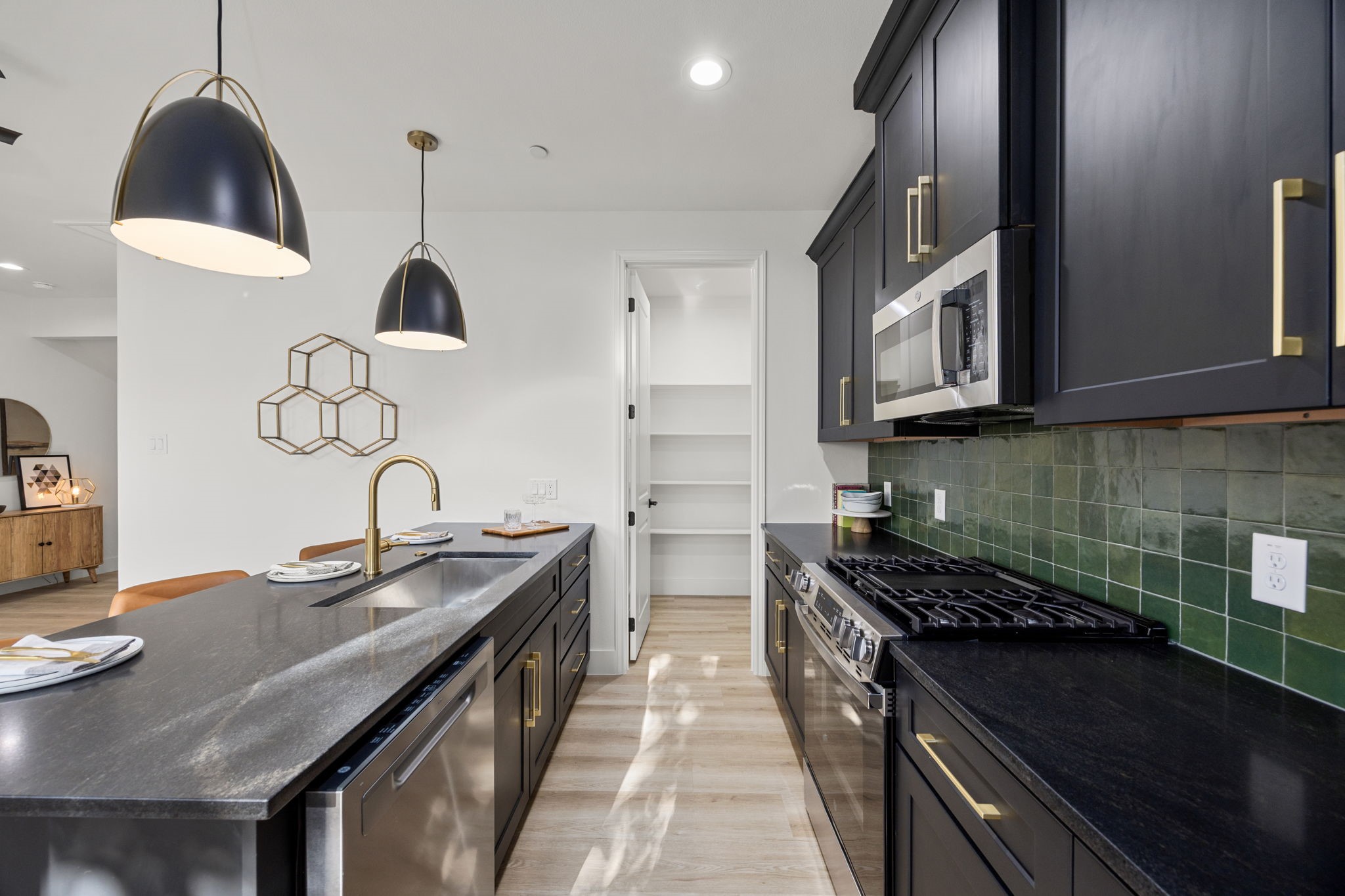 4611 Dewberry Street, Unit C Houston, TX 77021 - Photo 5 of 34 This modern kitchen features sleek black cabinetry with gold accents, a stylish green tile backsplash, and stainless steel appliances. The spacious island includes a sink and seating, illuminated by elegant pendant lights. A walk-in pantry offers ample storage space.