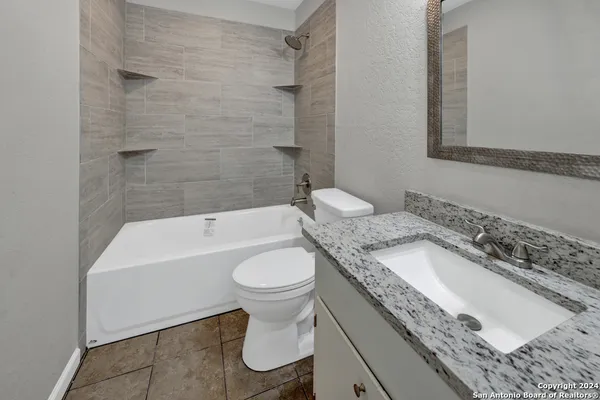 a bathroom with a granite countertop sink a toilet a mirror and bathtub