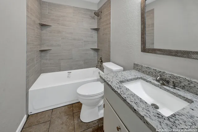 a bathroom with a granite countertop sink a toilet a mirror and bathtub