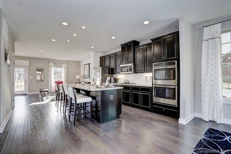 910 Portrush Lane, Unit 1015B Tega Cay, SC 29708 - Photo 3 of 8 a kitchen with stainless steel appliances kitchen island granite countertop a refrigerator a stove a sink a dining table and chairs with wooden floor