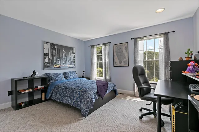 a bedroom with a bed a desk chair and windows