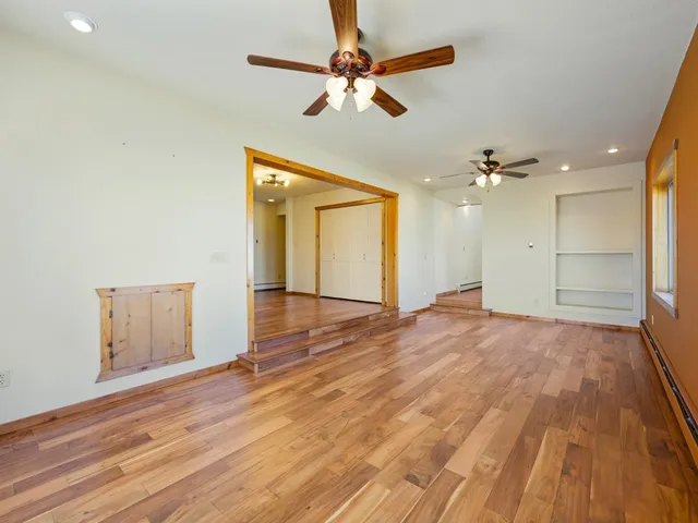 an empty room with wooden floor chandelier fan and windows