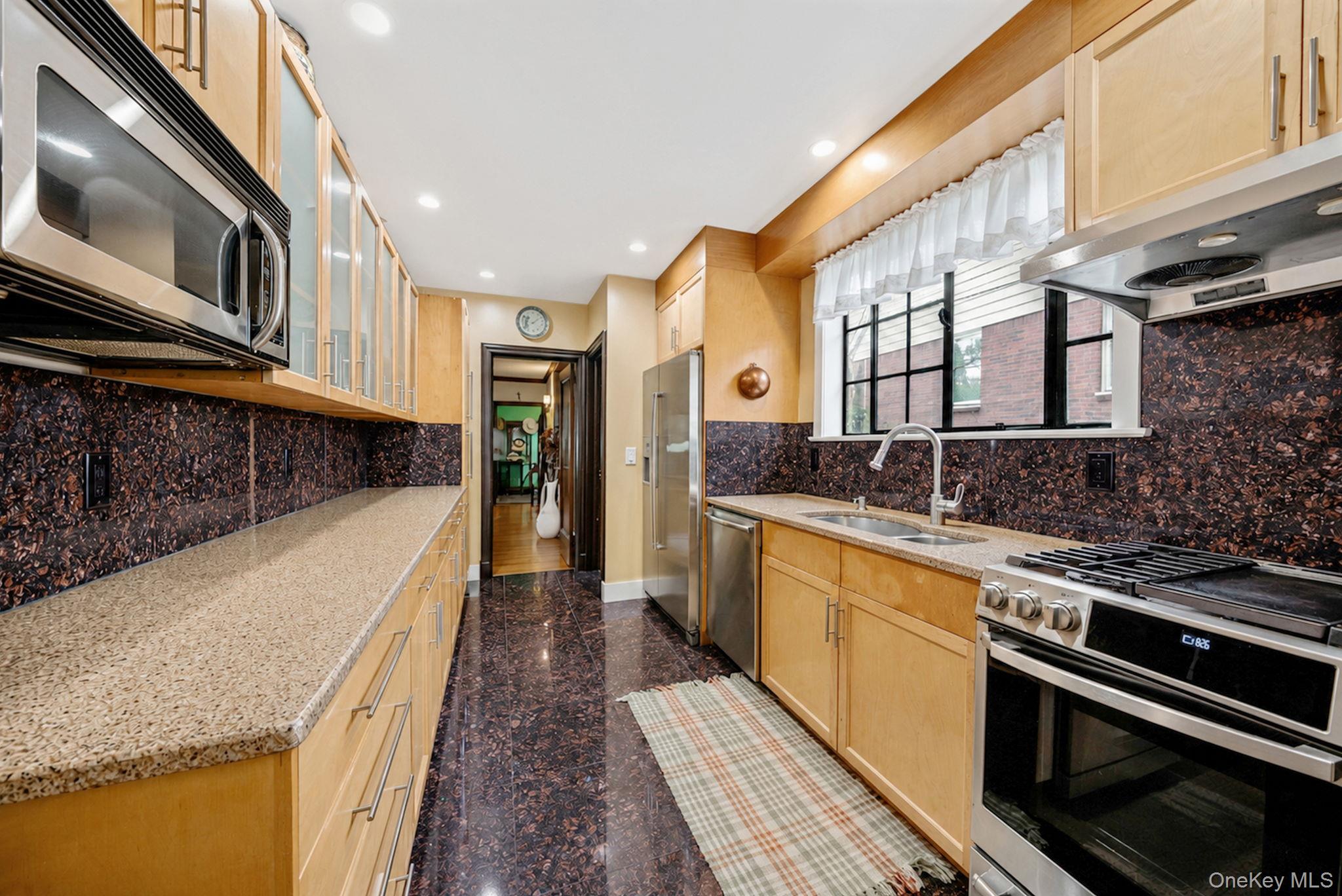 18240 Avon Road Queens, NY 11432 - Photo 14 of 30 Galley kitchen featuring light wood cabinetry, stone countertops, stainless steel appliances, and a dark stone backsplash
