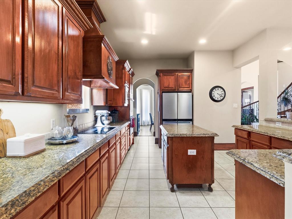 1615 Roma Lane Allen, TX 75013 - Photo 8 of 36 Spacious kitchen featuring extensive wood cabinetry, granite countertops, tile flooring, a central island, and stainless steel appliances