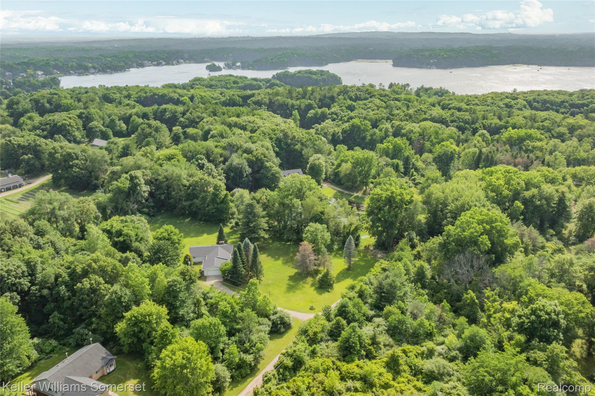 2344 Rochester Road Leonard, MI 48367 - Photo 63 of 66 Aerial perspective of a property nestled within a wooded landscape, featuring a large body of water in the background