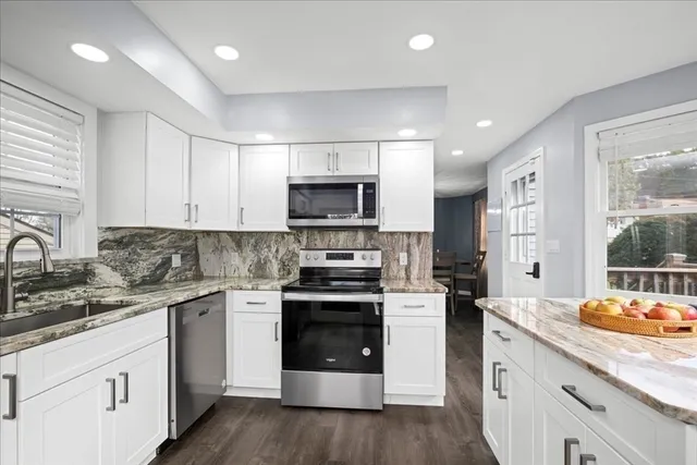 a kitchen with stainless steel appliances granite countertop a stove a sink dishwasher a refrigerator and white cabinets with wooden floor