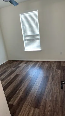 a view of an empty room with wooden floor and a window
