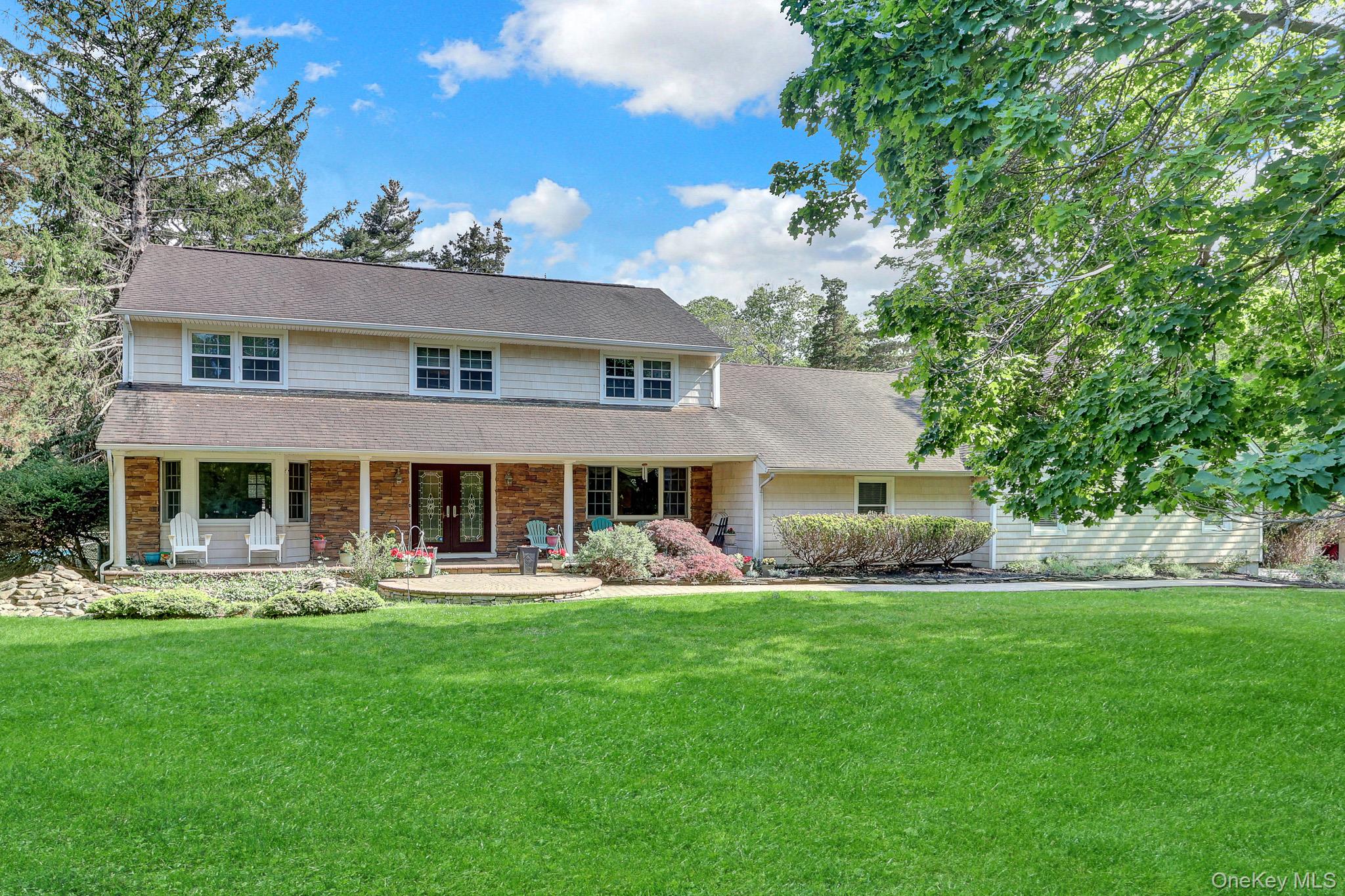 15 Stillwater Road Nissequogue, NY 11780 - Photo 1 of 43 Expansive green lawn fronts a two-story residence featuring light-colored siding and a covered front porch with stone facade accents
