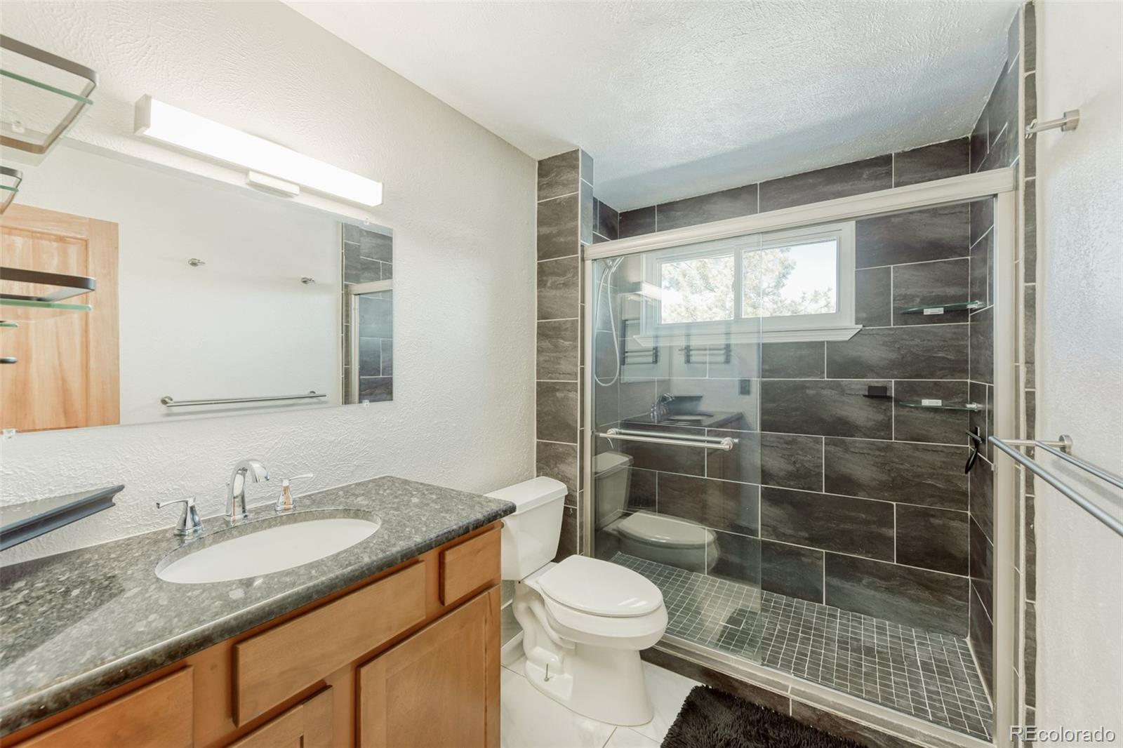 128 Olympus Circle Lone Tree, CO 80124 - Photo 27 of 35 a bathroom with a granite countertop sink a toilet a mirror and shower