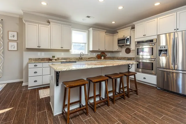 a kitchen with stainless steel appliances granite countertop a stove a sink dishwasher a refrigerator white cabinets and wooden floor next to a window