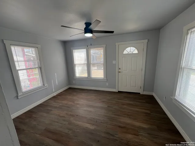 an empty room with wooden floor fan and windows