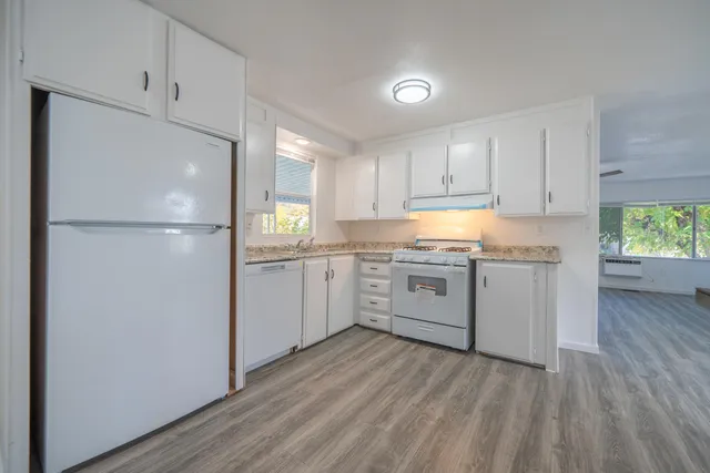 a kitchen with a white refrigerator oven a sink dishwasher and white cabinets with wooden floor