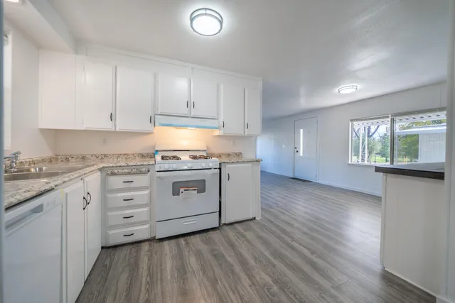 a kitchen with granite countertop white cabinets and white appliances with wooden floor