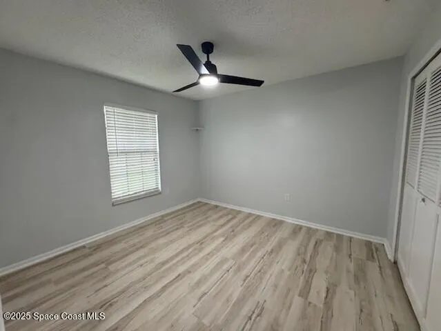 an empty room with wooden floor ceiling fan and windows