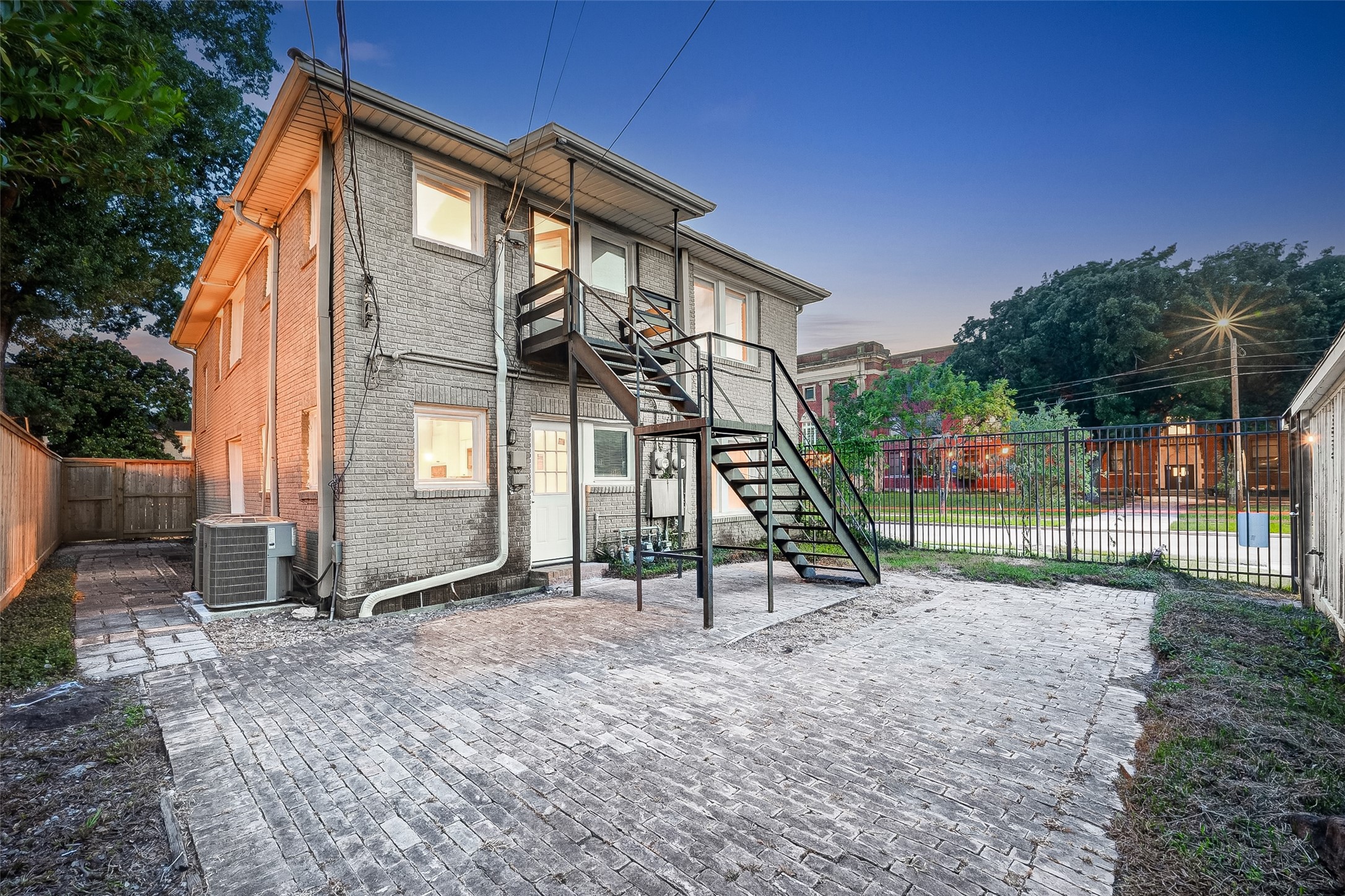 1758 Hawthorne Street, Unit 2 Houston, TX 77098 - Photo 17 of 19 This photo shows the back of a two-story brick home with an exterior staircase leading to the second floor. The yard is paved with bricks and enclosed by a fence, providing a private outdoor space.