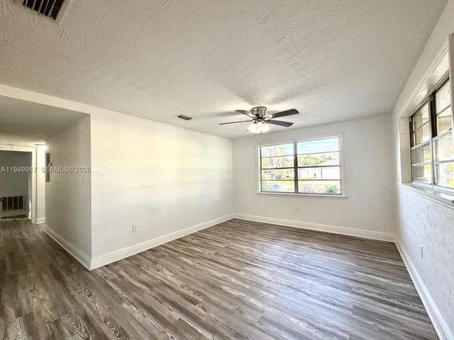 an empty room with wooden floor fan and windows