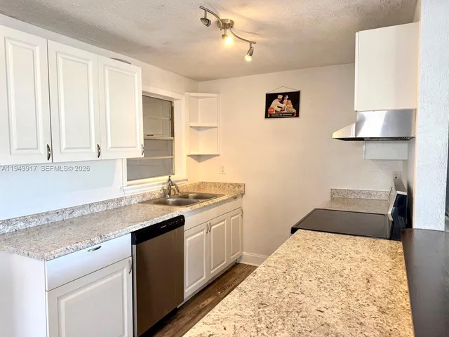 a kitchen with granite countertop a sink stainless steel appliances and white cabinets