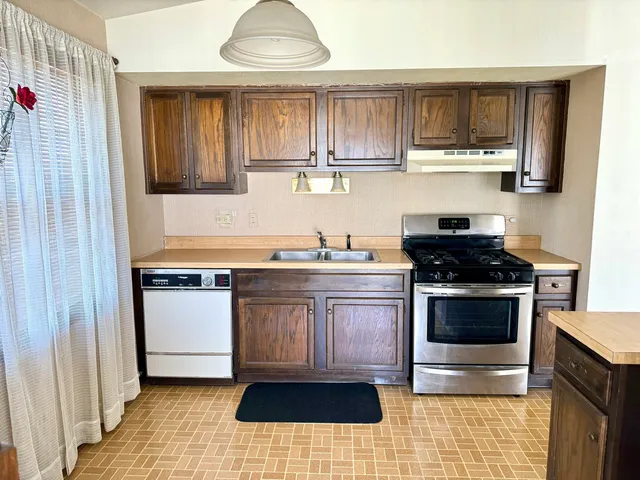 a kitchen with stainless steel appliances granite countertop a sink dishwasher a stove and a refrigerator with wooden floor