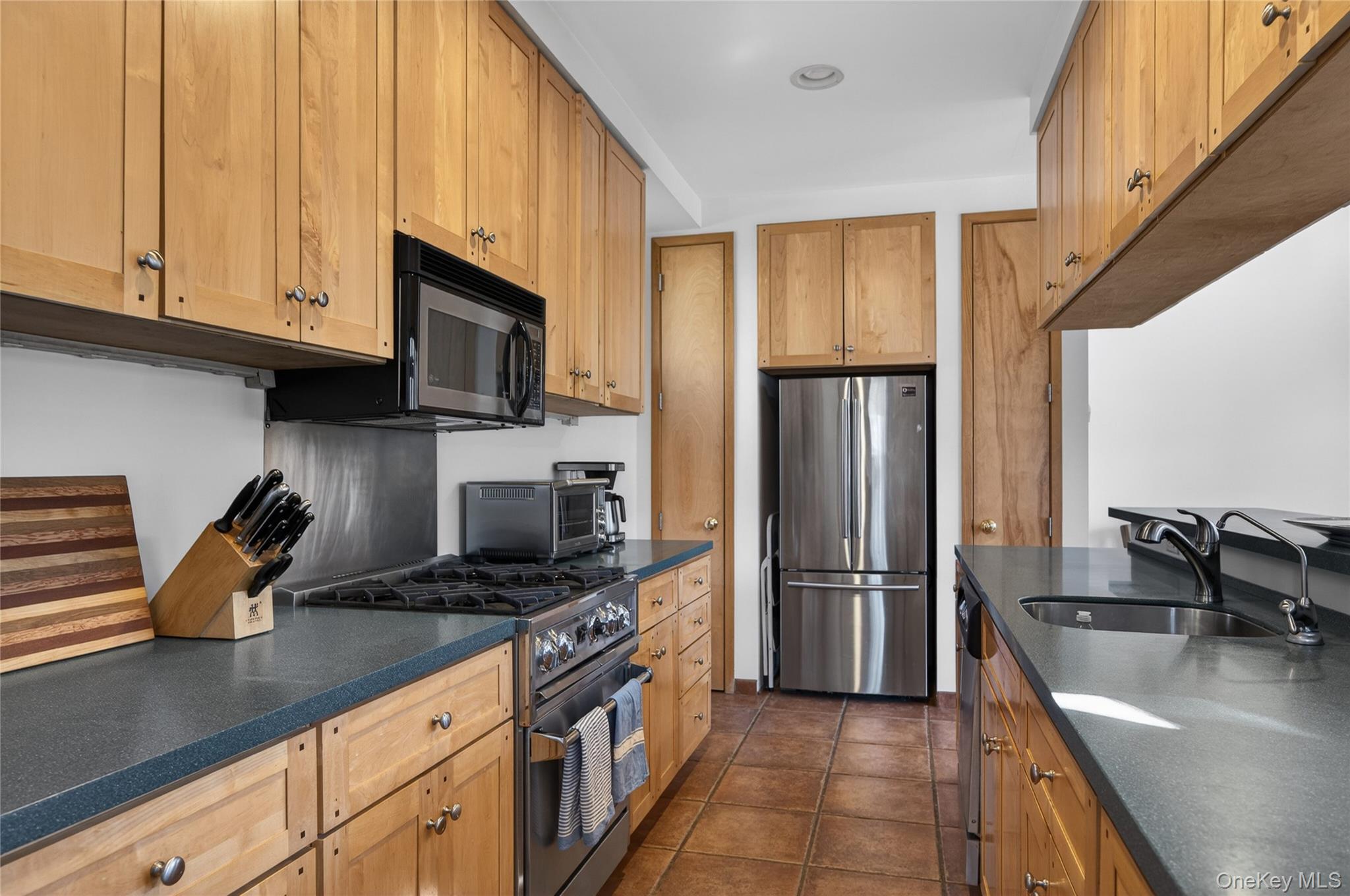 428 Harbor Road, Unit C Syosset, NY 11791 - Photo 9 of 29 Galley kitchen featuring natural wood cabinetry, dark countertops, stainless steel appliances, and tiled flooring