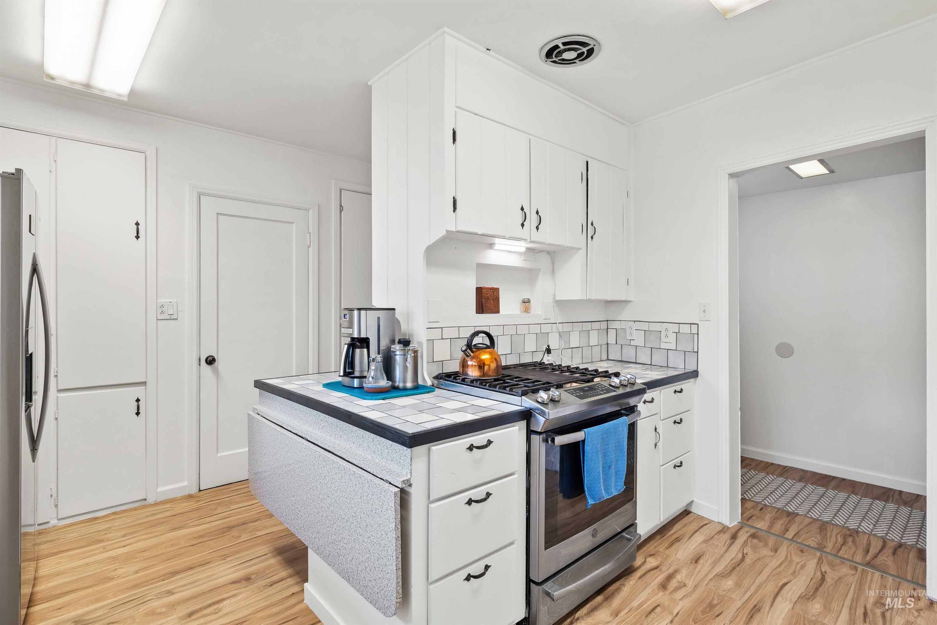 817 Union Avenue Filer, ID 83328 - Photo 10 of 37 Kitchen with tile countertops, white cabinetry, stainless steel appliances, light wood finished floors, and tasteful backsplash