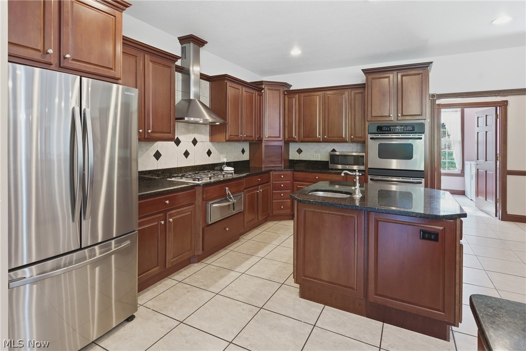 2184 Brenner Road Northeast Carrollton, OH 44615 - Photo 10 of 50 Kitchen featuring rich wood cabinetry, stainless steel appliances, granite countertops, a tiled backsplash, and a central island with an undermount sink