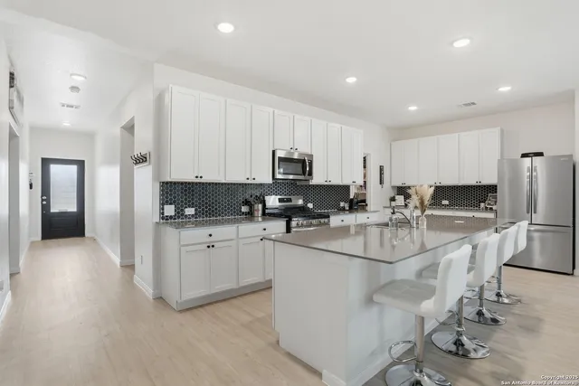 a kitchen with stainless steel appliances granite countertop a stove top oven a sink a refrigerator and white cabinets