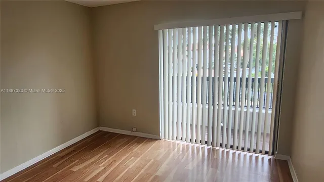 a view of an empty room with wooden floor and a bathroom