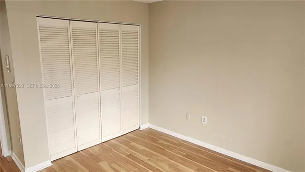 a view of an empty room with wooden floor and a bathroom