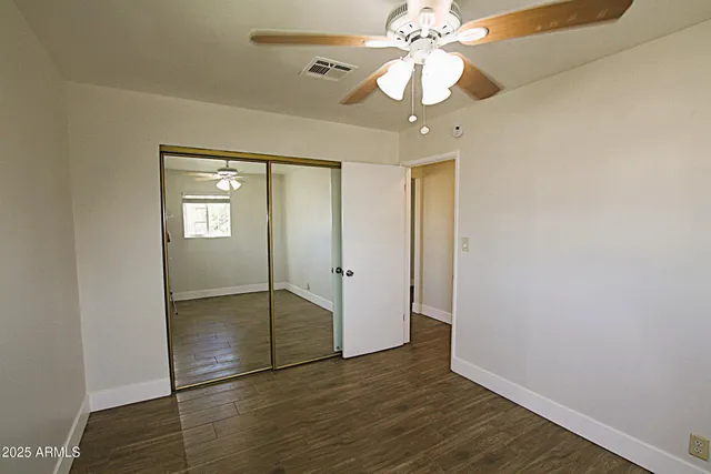 a view of an empty room with wooden floor and a ceiling fan